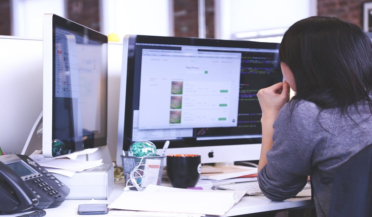 Long-Haired Person Looking At Two Imac Computers On A Desktop