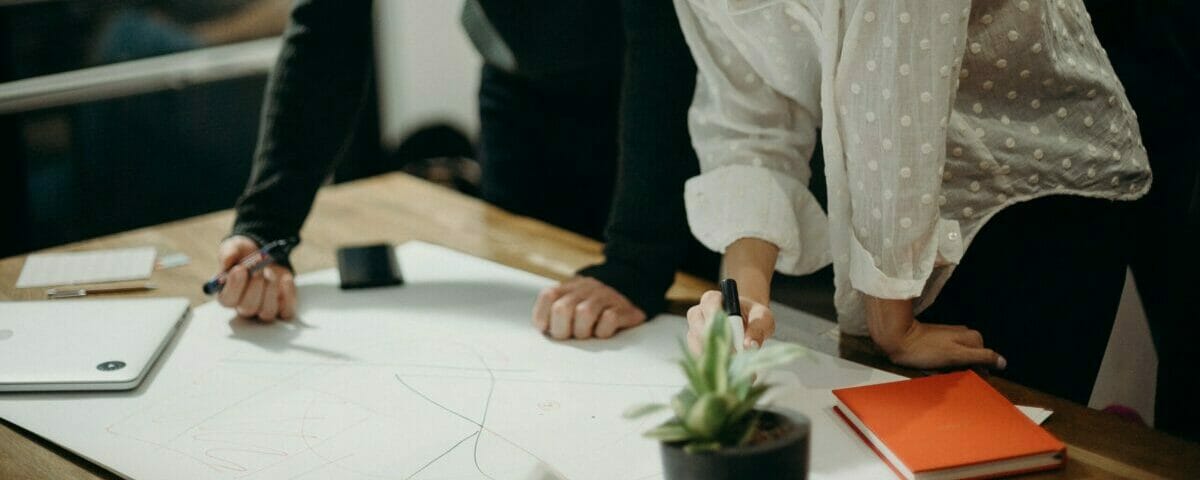 Man And Woman Leaning On Table Staring At White Board On Top Of Table Having A Meeting